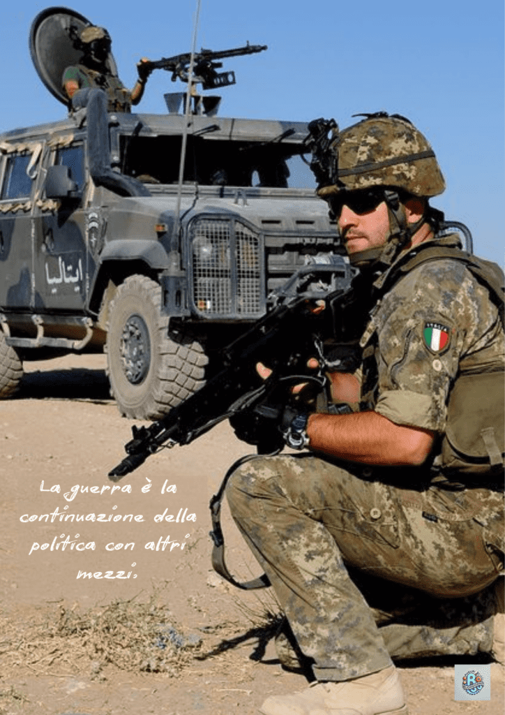 Un soldato italiano in missione, accovacciato con il fucile, mentre un veicolo blindato è visibile sullo sfondo. La citazione "La guerra è la continuazione della politica con altri mezzi" riflette l'interconnessione tra conflitto e decisioni politiche, un tema commemorato nella Giornata dell'Unità Nazionale e delle Forze Armate.