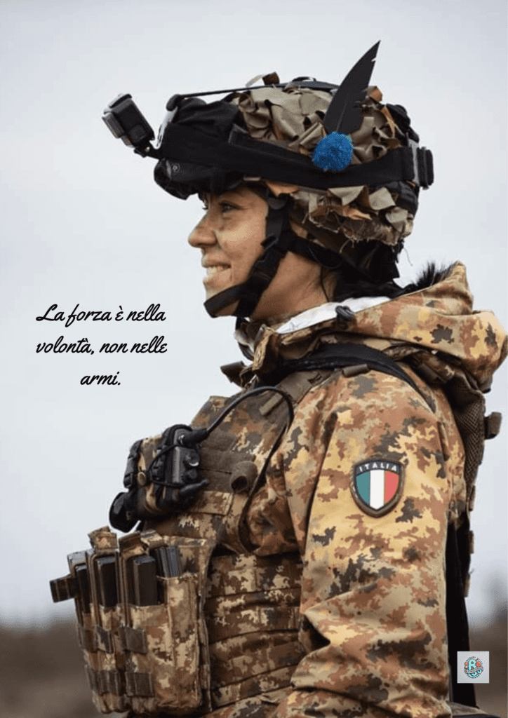 Una soldatessa italiana sorridente, in tenuta militare, con il casco e gli accessori da campo. La citazione "La forza è nella volontà, non nelle armi" enfatizza il potere della determinazione rispetto alla semplice potenza delle armi, in occasione della Giornata dell'Unità Nazionale e delle Forze Armate.